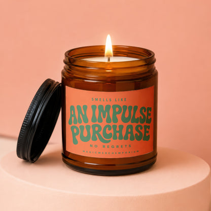 Amber candle with lit wick and open lid, reads "Smells Like An Impulse Purchase"