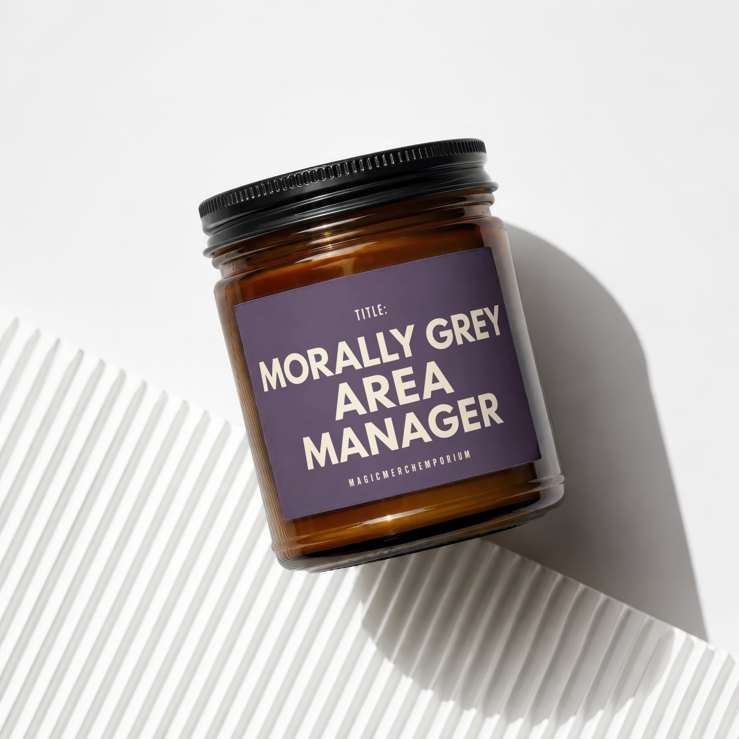 Amber candle in glass jar with black lid, white text "TITLE: MORALLY GREY AREA MANAGER".