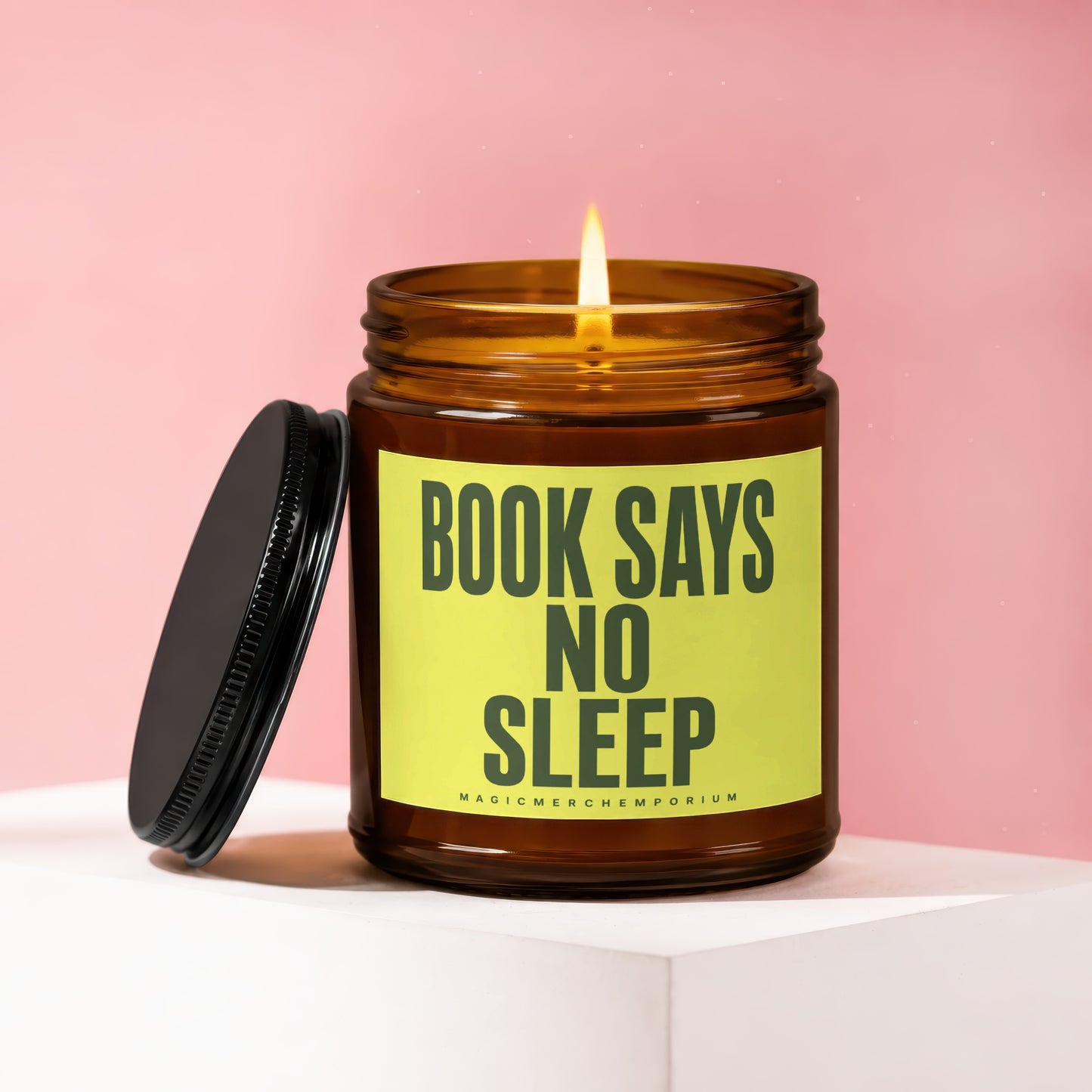 Lit amber glass candle with "BOOK SAYS NO SLEEP" on a yellow label.