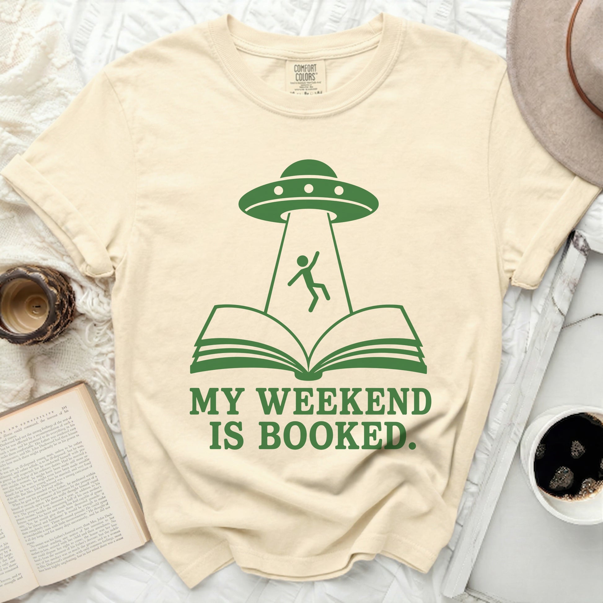 Cream t-shirt with green UFO abducting person from open book, text says "MY WEEKEND IS BOOKED."