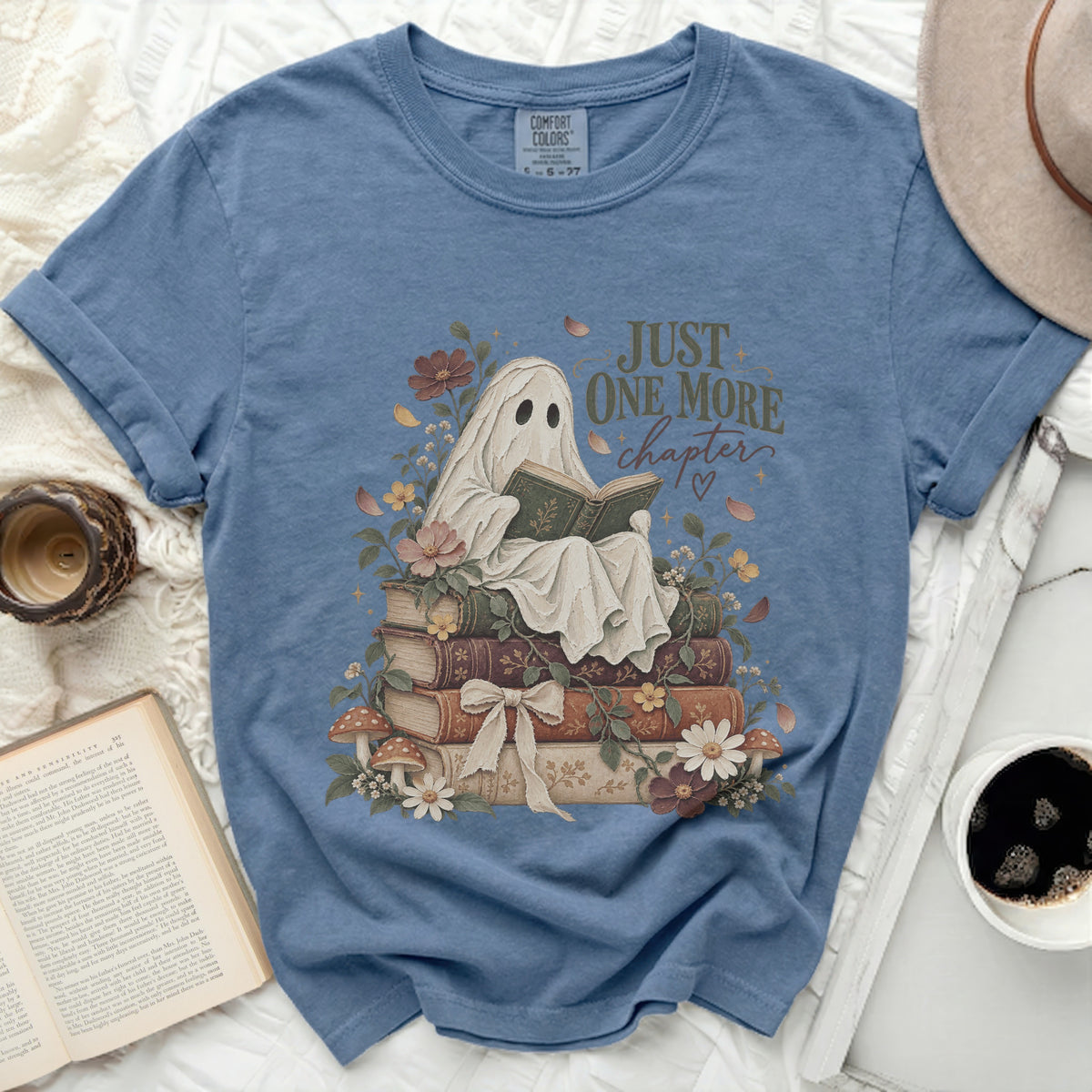 Blue t-shirt with ghost reading book on stack of books, text "Just One More Chapter".