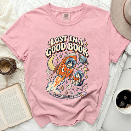Pink t-shirt with graphic of cats, rocket, moon, stars, and text "LOST IN A GOOD BOOK".