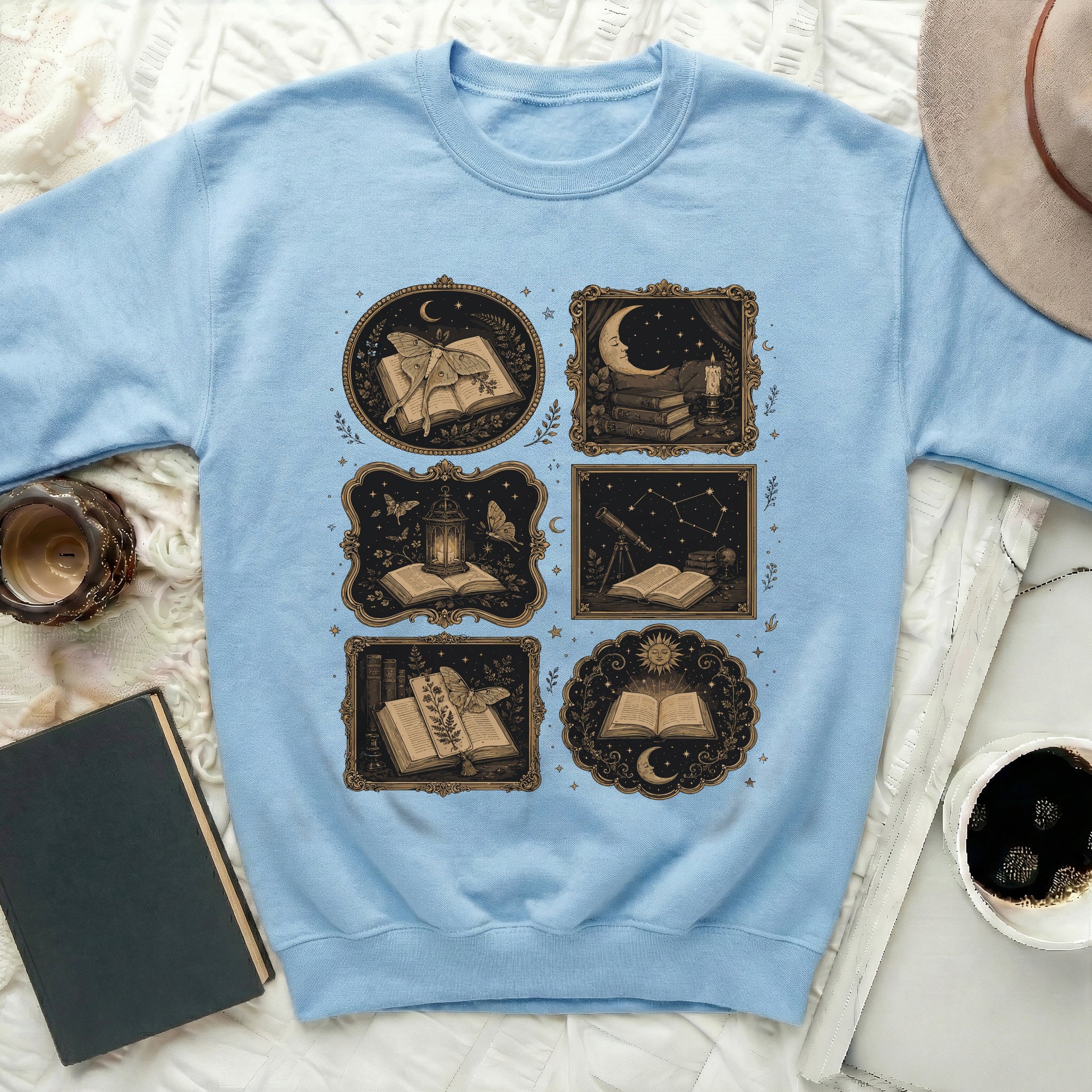 Light blue sweatshirt with a collage of six vintage-style illustrations of books and celestial elements.