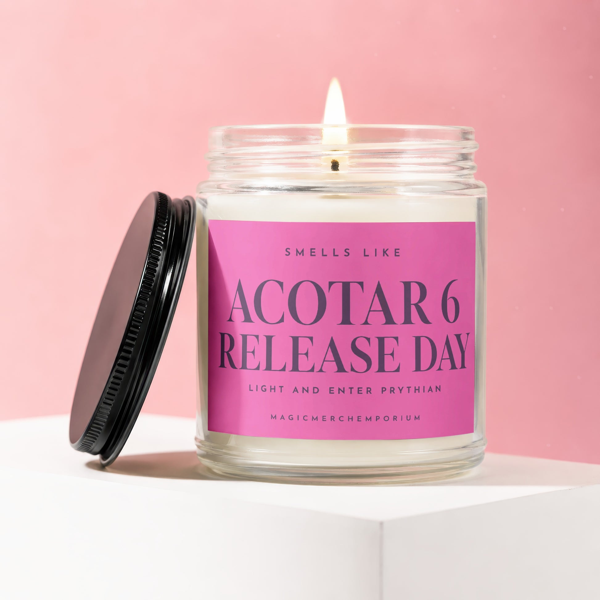 A lit candle in a clear glass jar with a pink label reading Acotar 6 Release Day.
