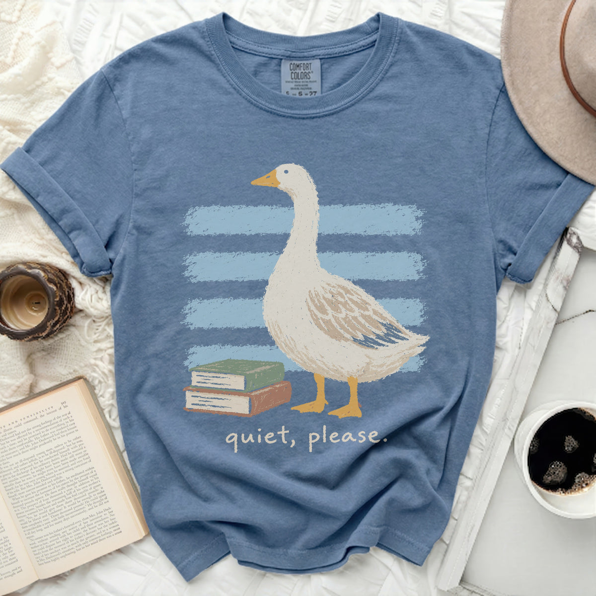Blue t-shirt with graphic of a goose and books, reads "quiet, please."