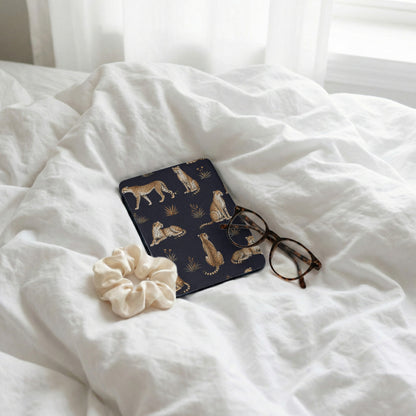 Dark blue case with cheetah pattern, glasses, and scrunchie on white bedding.