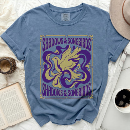 Blue t-shirt with a yellow bird and purple swirls graphic and "Shadows & Songbirds" text.