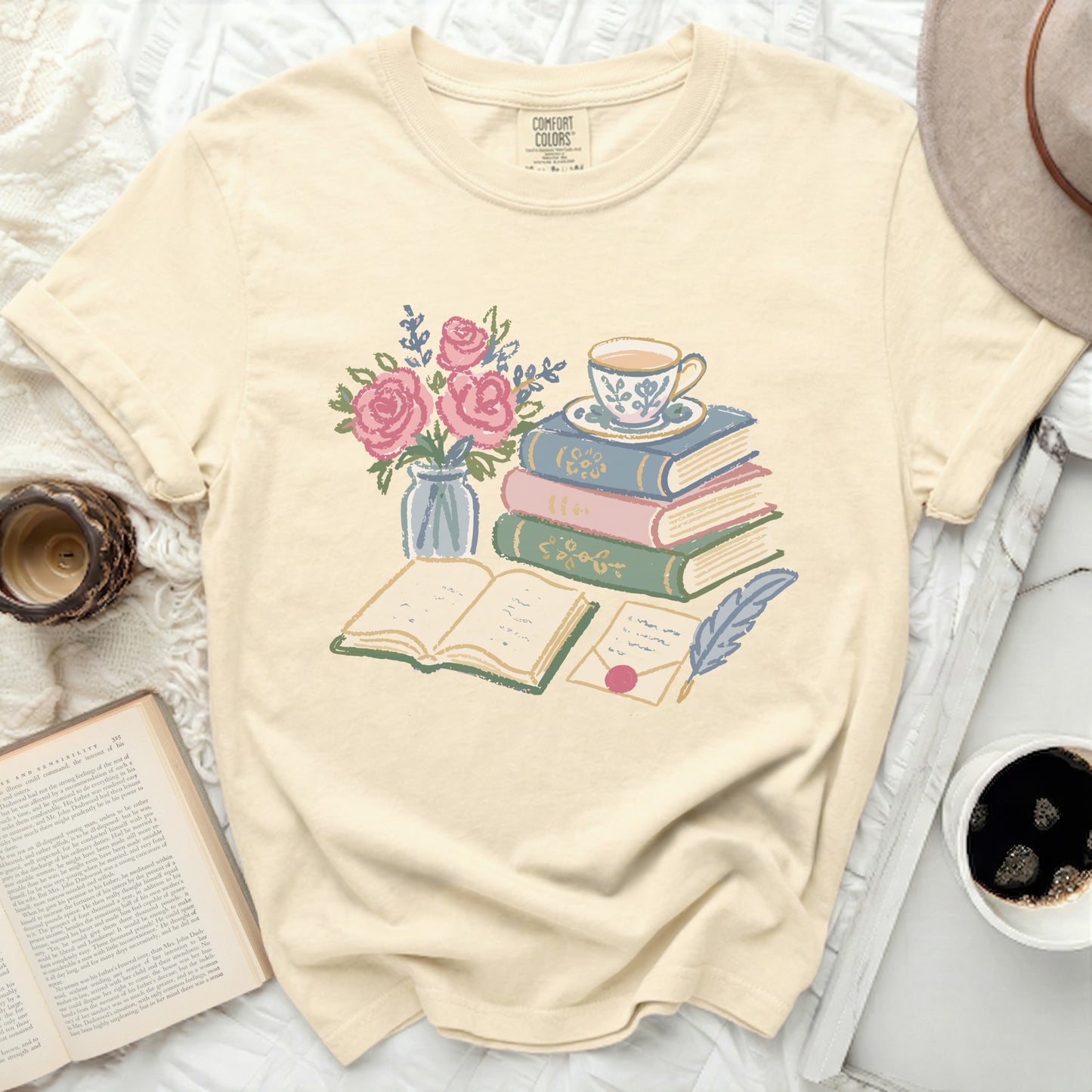 Cream t-shirt with illustration of stacked books, tea cup, roses, and feather quill.