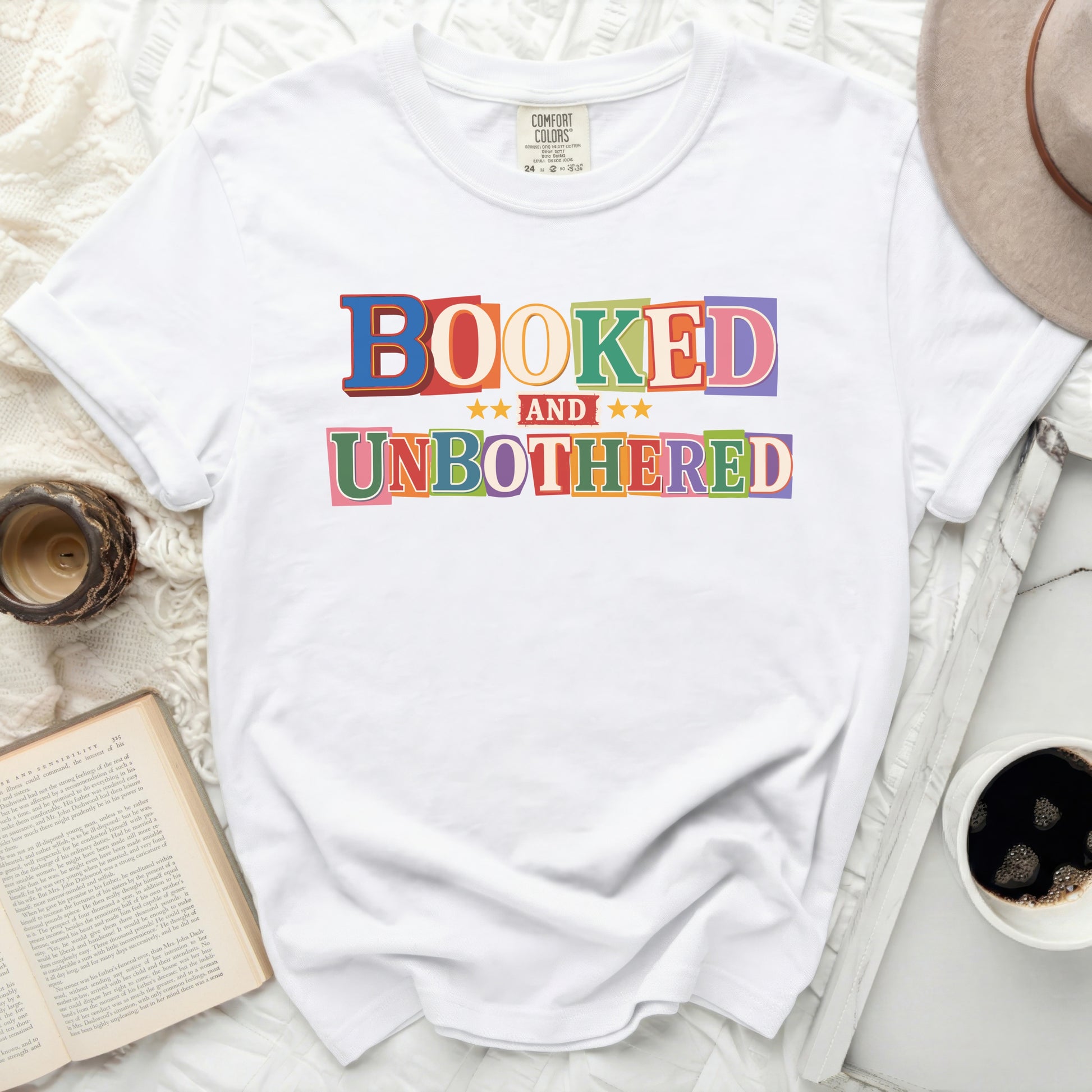 White t-shirt with colorful "BOOKED AND UNBOTHERED" text graphic.