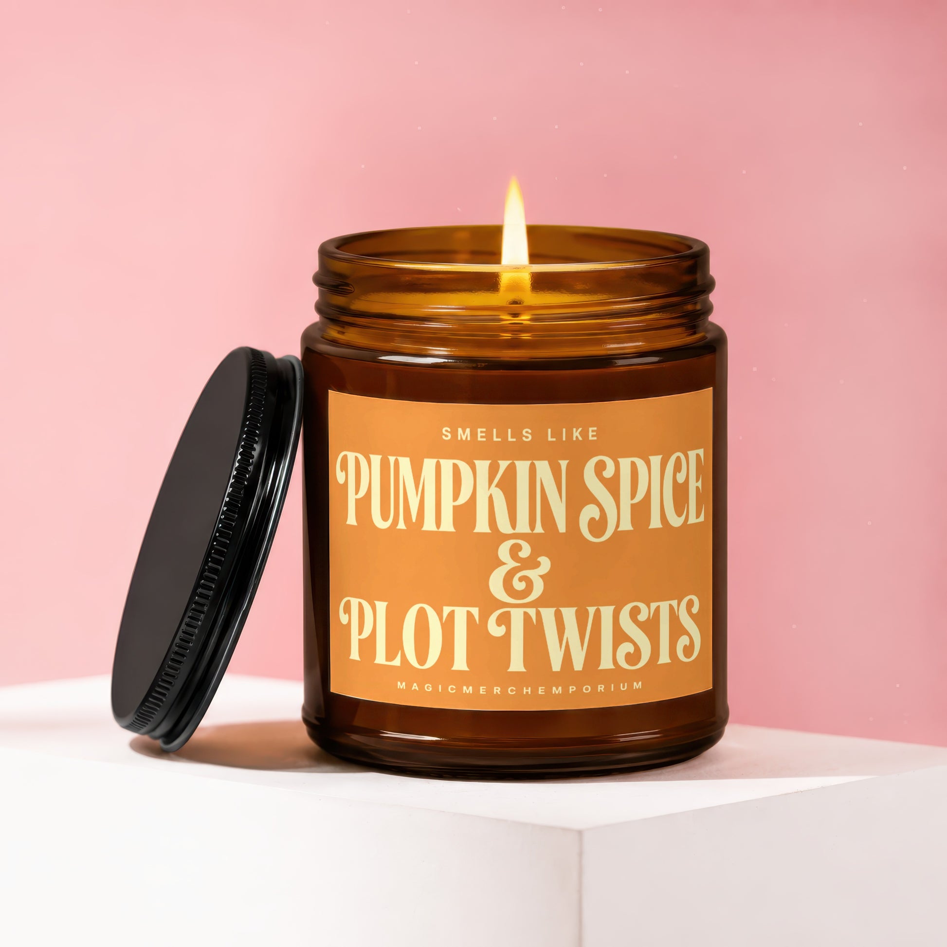 Amber jar candle with lit wick, reads "Smells Like Pumpkin Spice & Plot Twists".