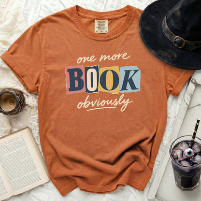 Orange t-shirt with "one more BOOK obviously" graphic and a witch hat.