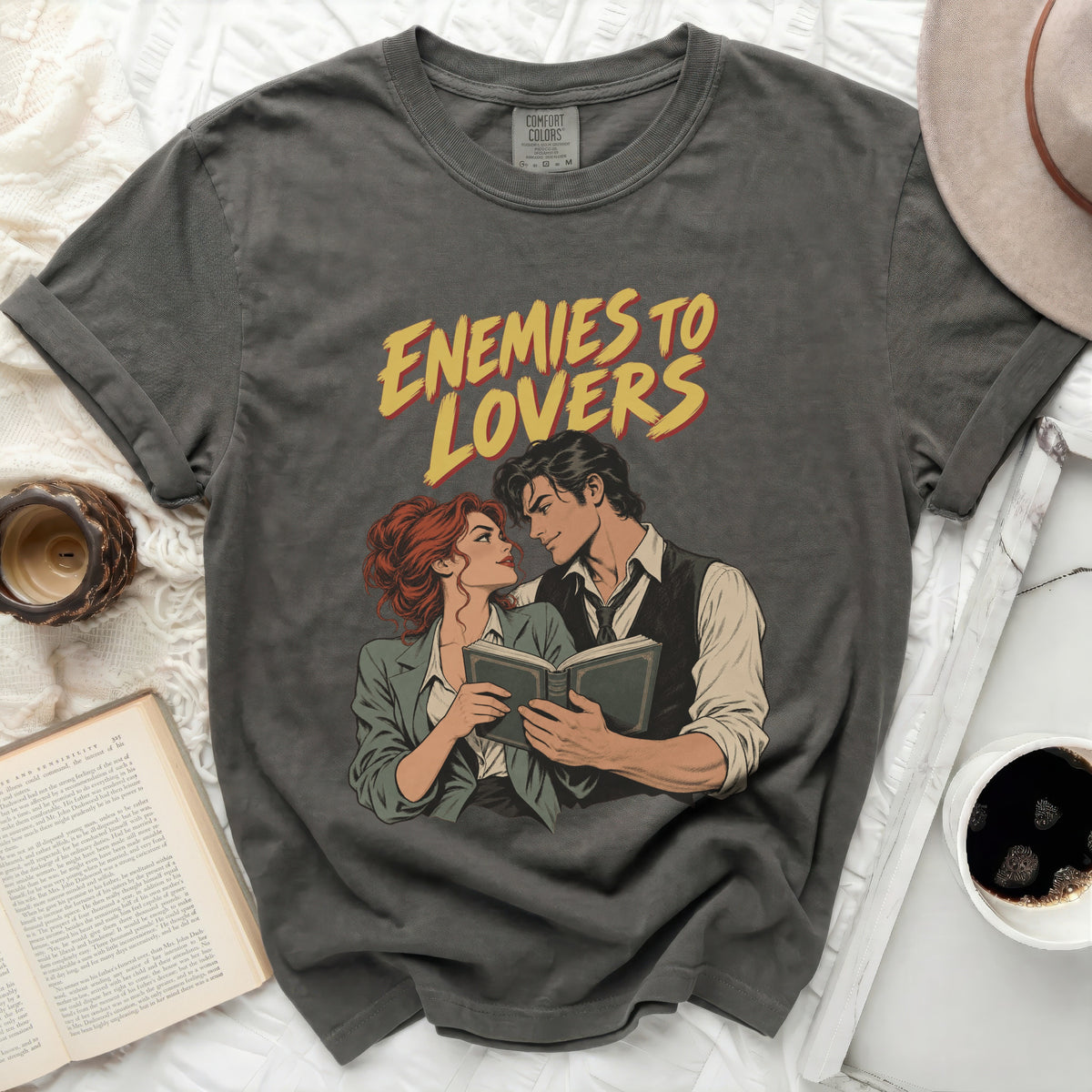 T-shirt with graphic art of a couple reading and "Enemies to Lovers" text.