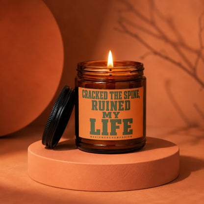 Amber jar candle with lit flame, reading "Cracked the spine, ruined my life."