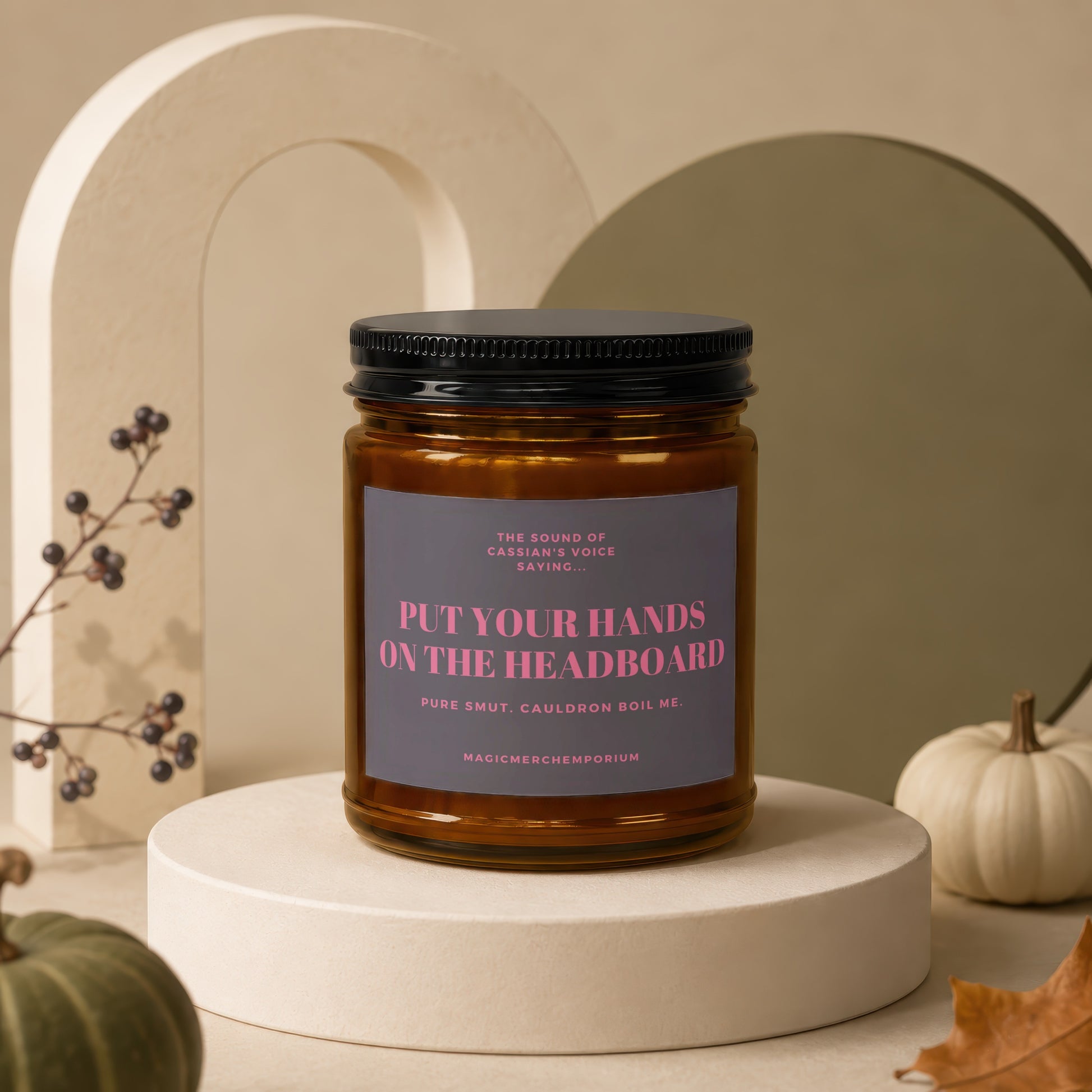 Amber candle with black lid, grey label reading "Put Your Hands On The Headboard".