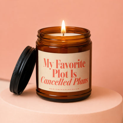 Amber jar candle with lit flame, reading "My Favorite Plot Is Cancelled Plans".