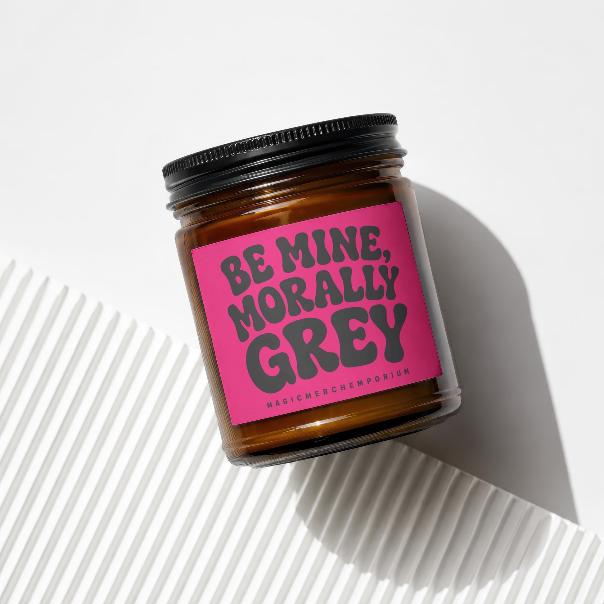 Brown glass candle with pink label that reads "BE MINE, MORALLY GREY".