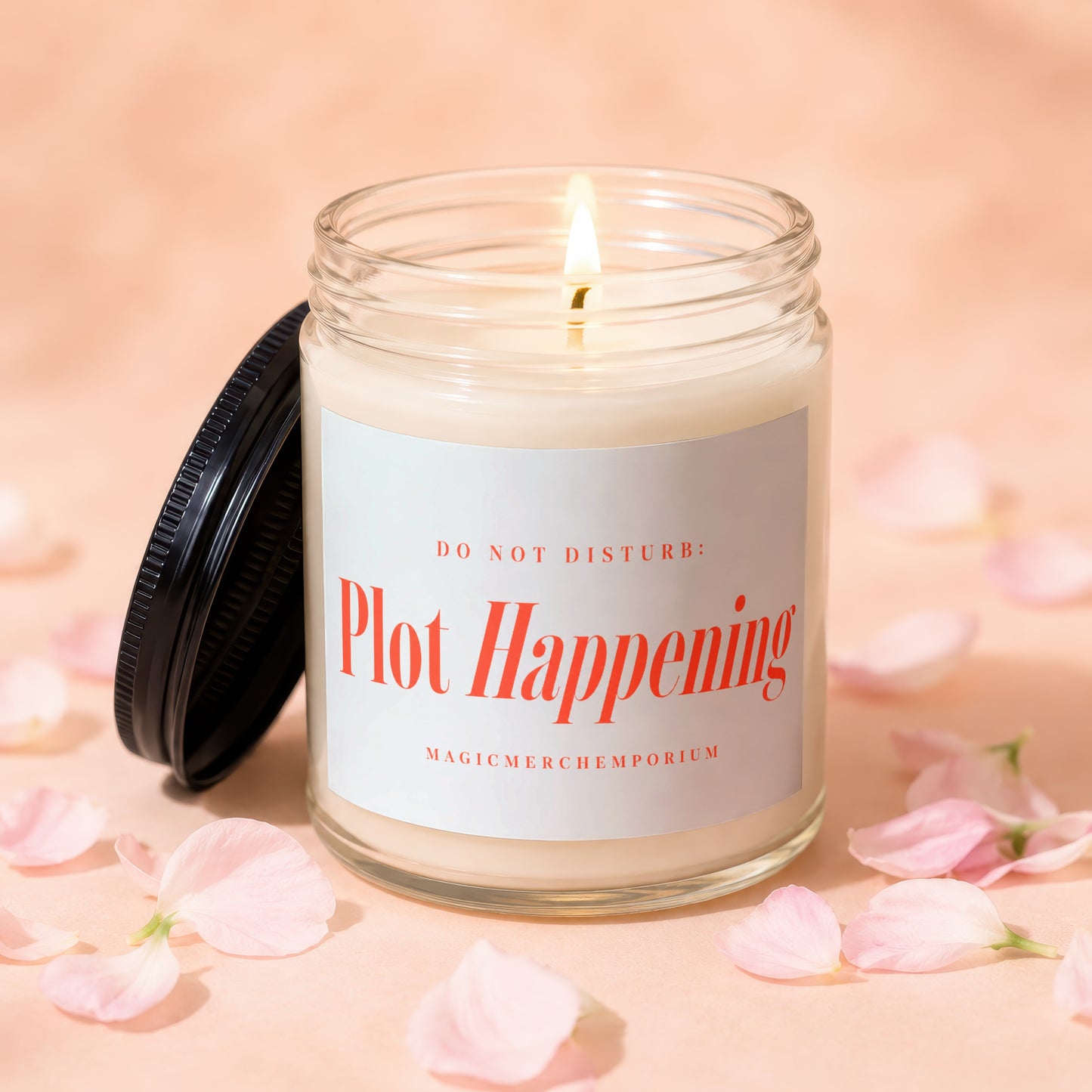Lit candle in glass jar with "Plot Happening" text, surrounded by pink petals.
