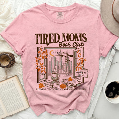 Pink t-shirt with "Tired Moms Book Club" and autumn cityscape graphic.