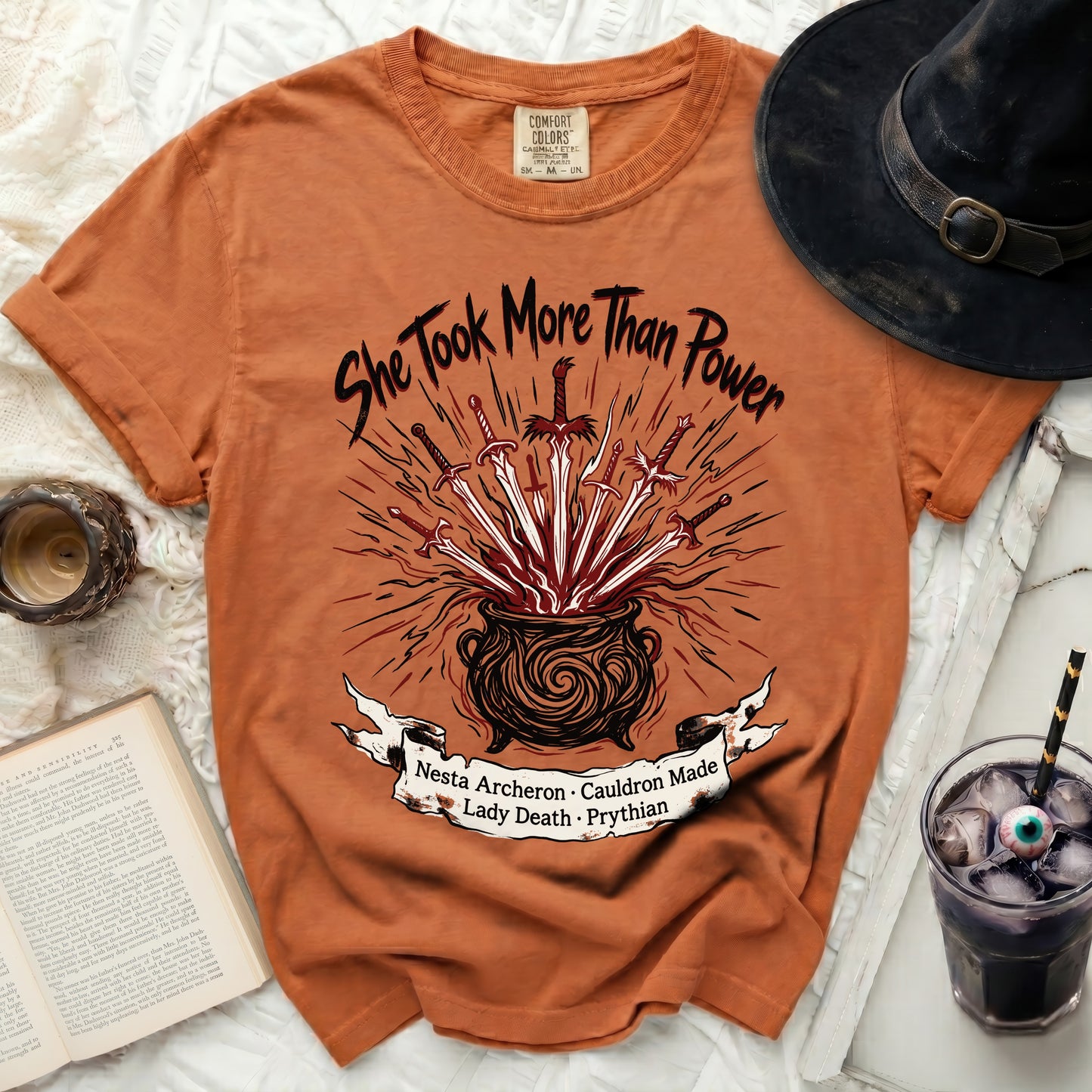 Orange t-shirt with "She Took More Than Power" and cauldron graphic.