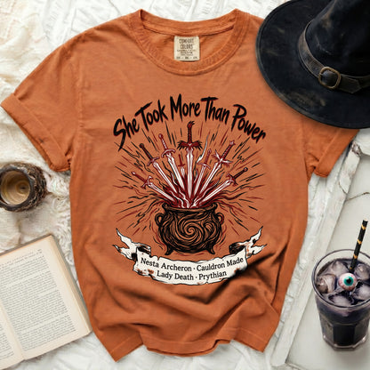 Orange t-shirt with "She Took More Than Power" and cauldron graphic.