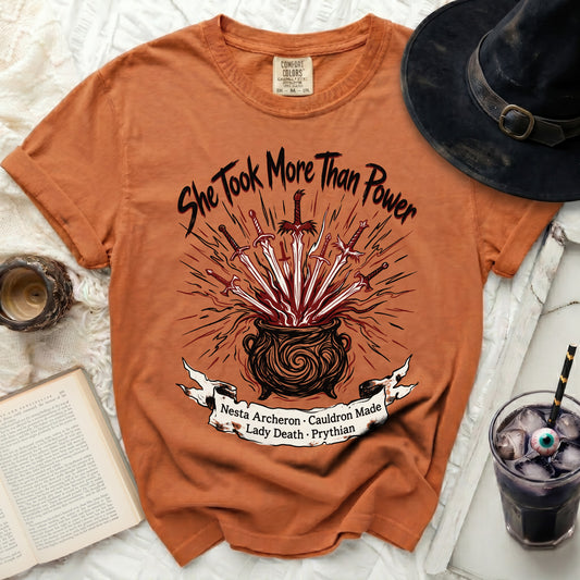 Orange t-shirt with "She Took More Than Power" and cauldron graphic.