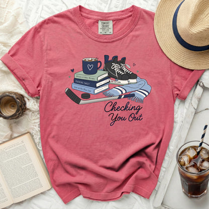 Pink t-shirt with hockey skates, puck, stick, and scarf graphic and text.