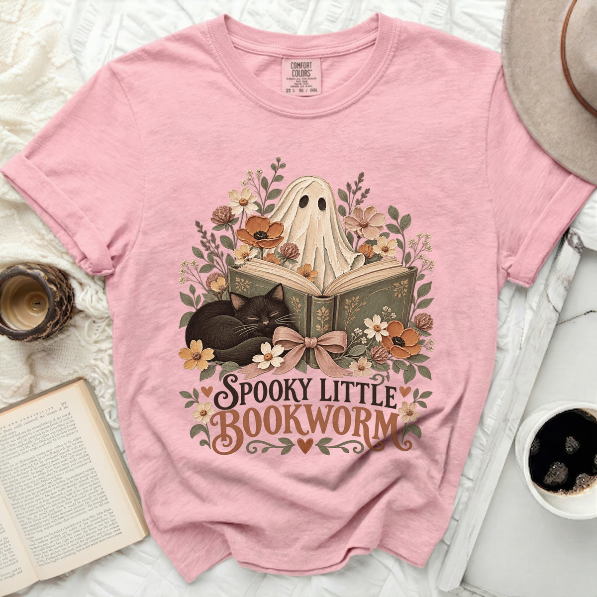Pink Comfort Colors shirt with a ghost, cat, and books graphic reading "Spooky Little Bookworm".