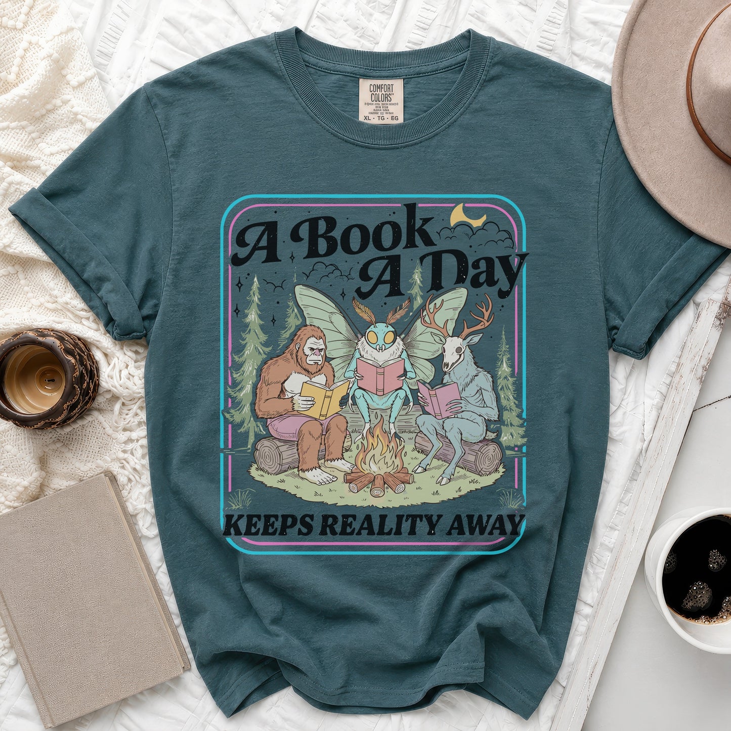 Graphic t-shirt with "A Book A Day Keeps Reality Away" text and forest creatures reading.