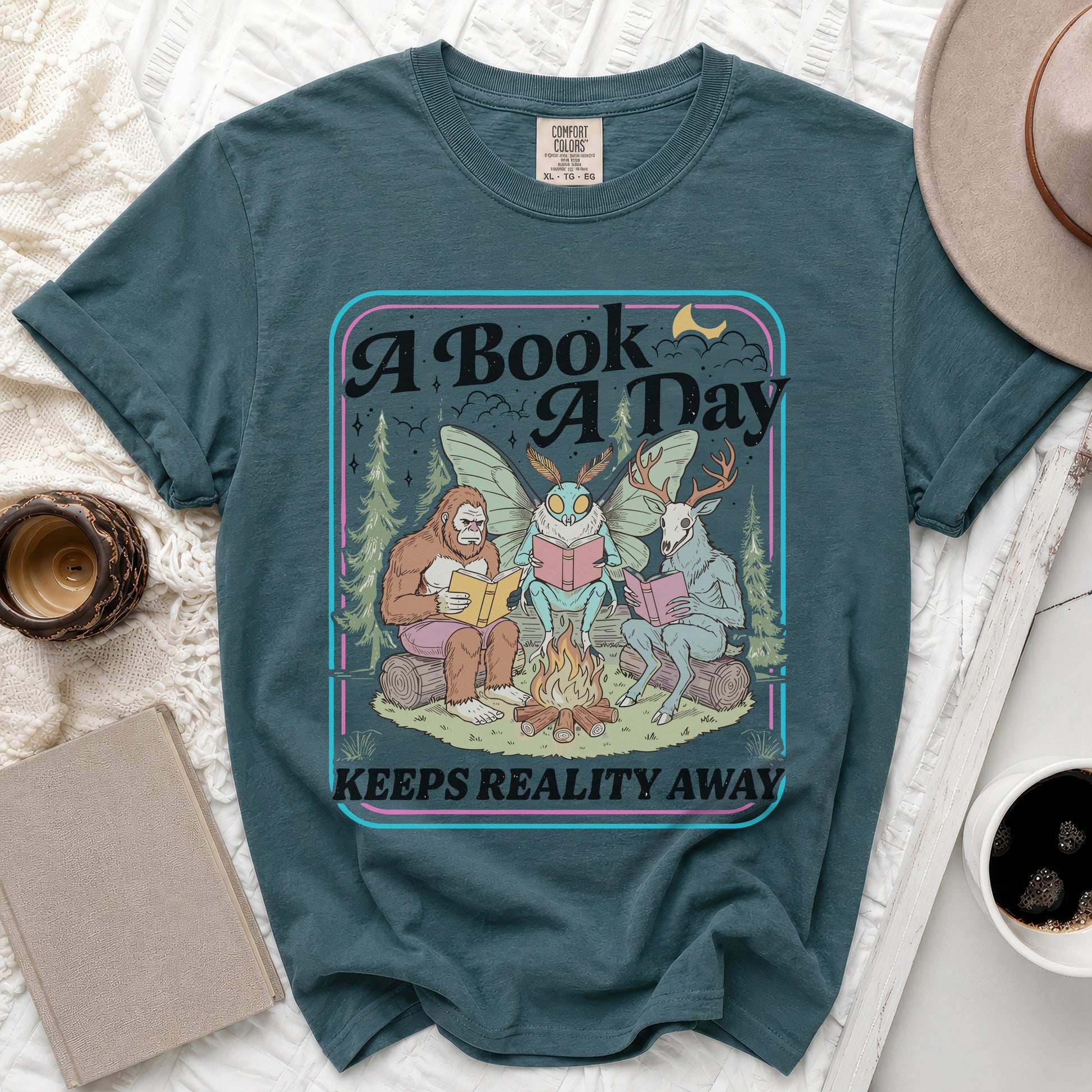Graphic t-shirt with "A Book A Day Keeps Reality Away" text and forest creatures reading.
