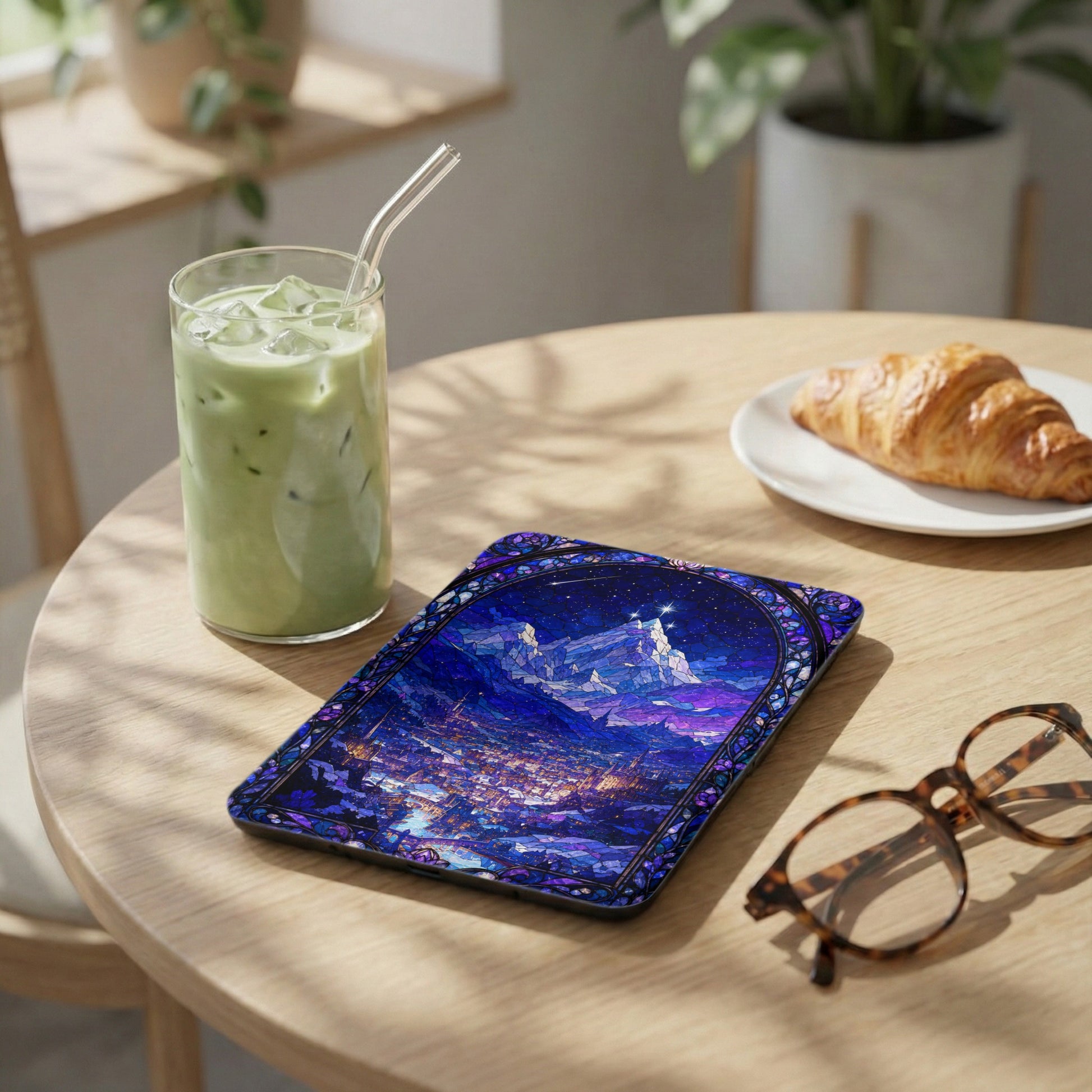 Tablet with stained glass art of a starry sky and city on a wooden table.