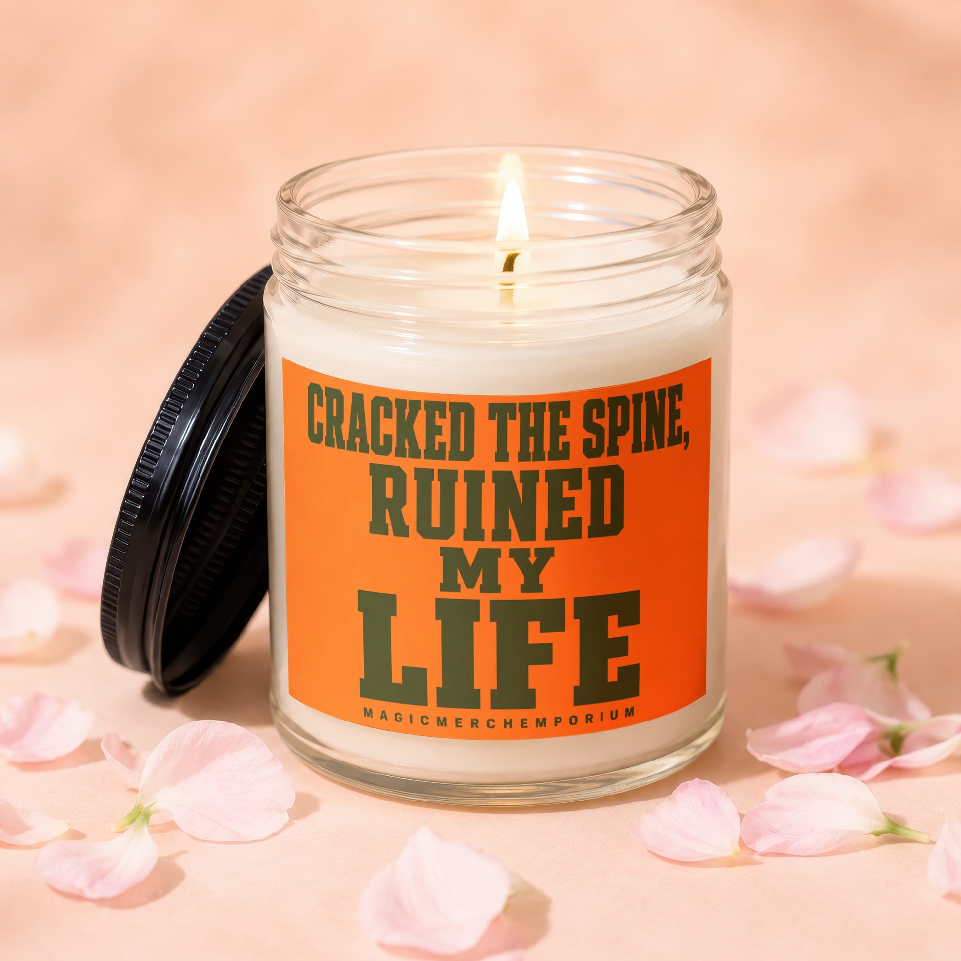 Lit candle in a jar with orange label reading "Cracked the Spine, Ruined My Life."