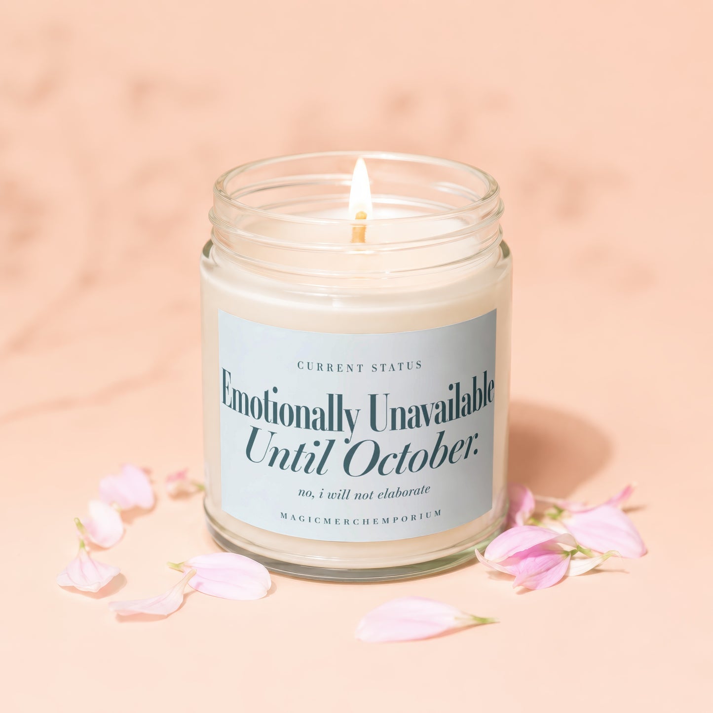 Glass candle with lit wick, label reads "Emotionally Unavailable Until October."