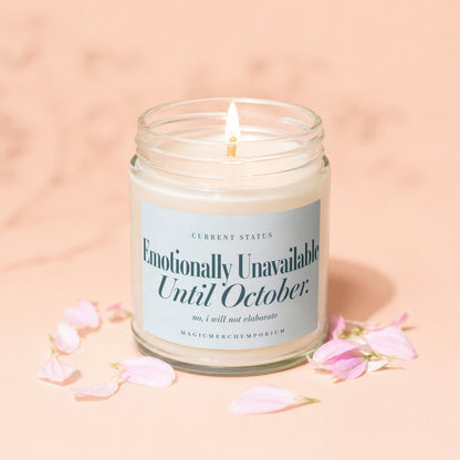 Glass candle with lit wick, label reads "Emotionally Unavailable Until October."