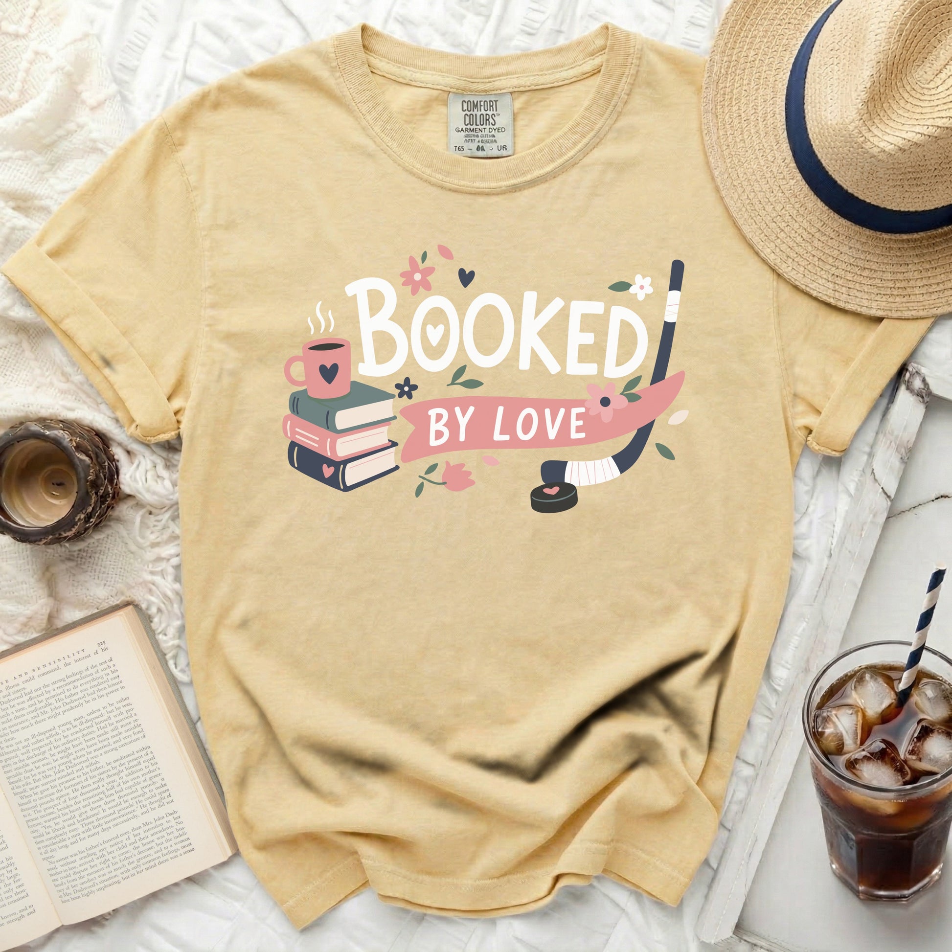 Yellow t-shirt with "Booked By Love" text, books, and hockey stick.
