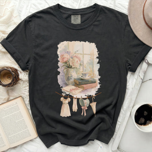 Black t-shirt with print of washing line with clothes, books, and flowers.