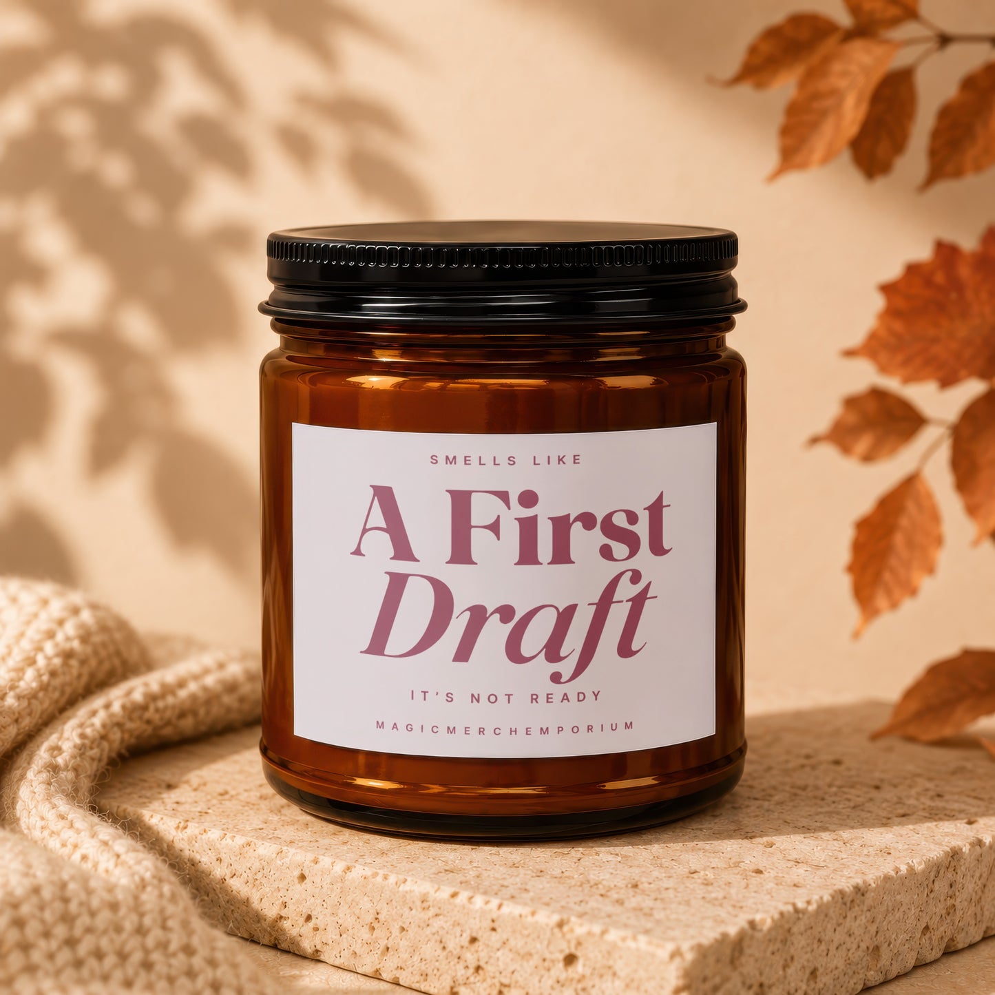 Brown jar candle, "A First Draft" text, with knit fabric and leaves.