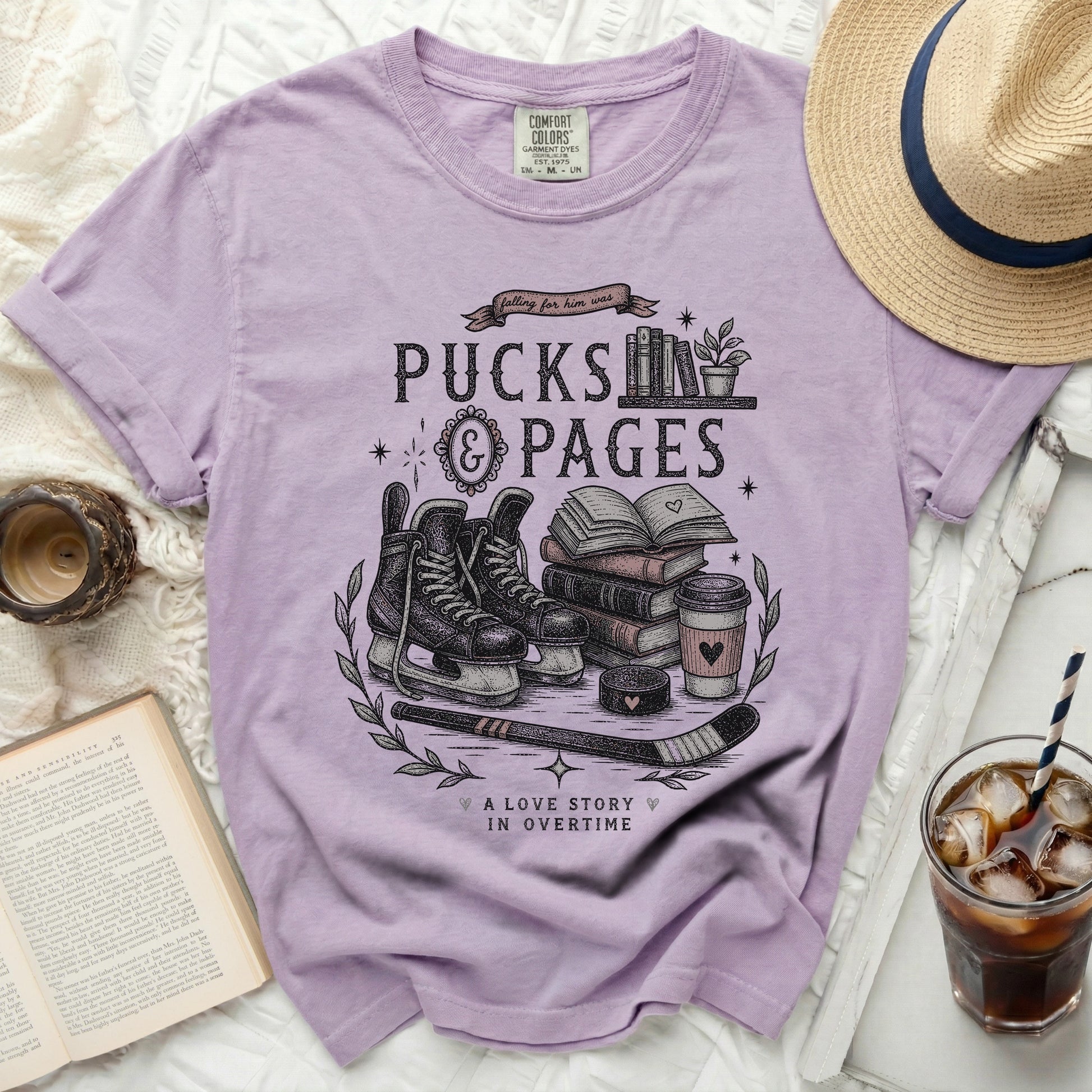 Purple t-shirt with "Pucks & Pages" design featuring skates, books, and coffee cup.