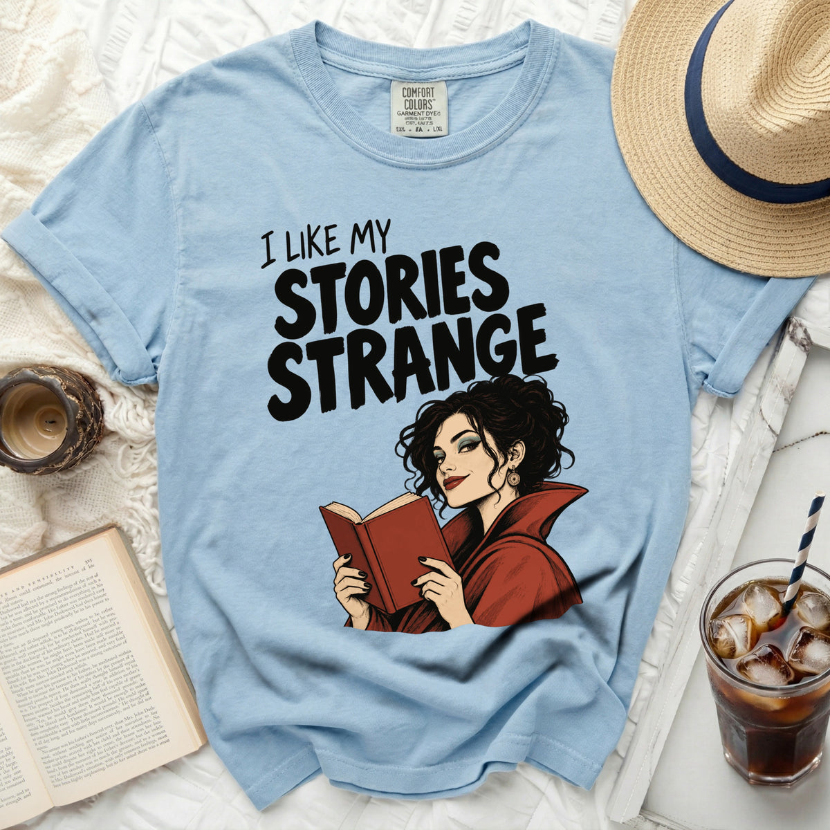 Light blue t-shirt with "I LIKE MY STORIES STRANGE" graphic and a woman reading.