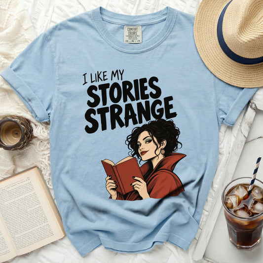 Light blue t-shirt with "I LIKE MY STORIES STRANGE" graphic and a woman reading.