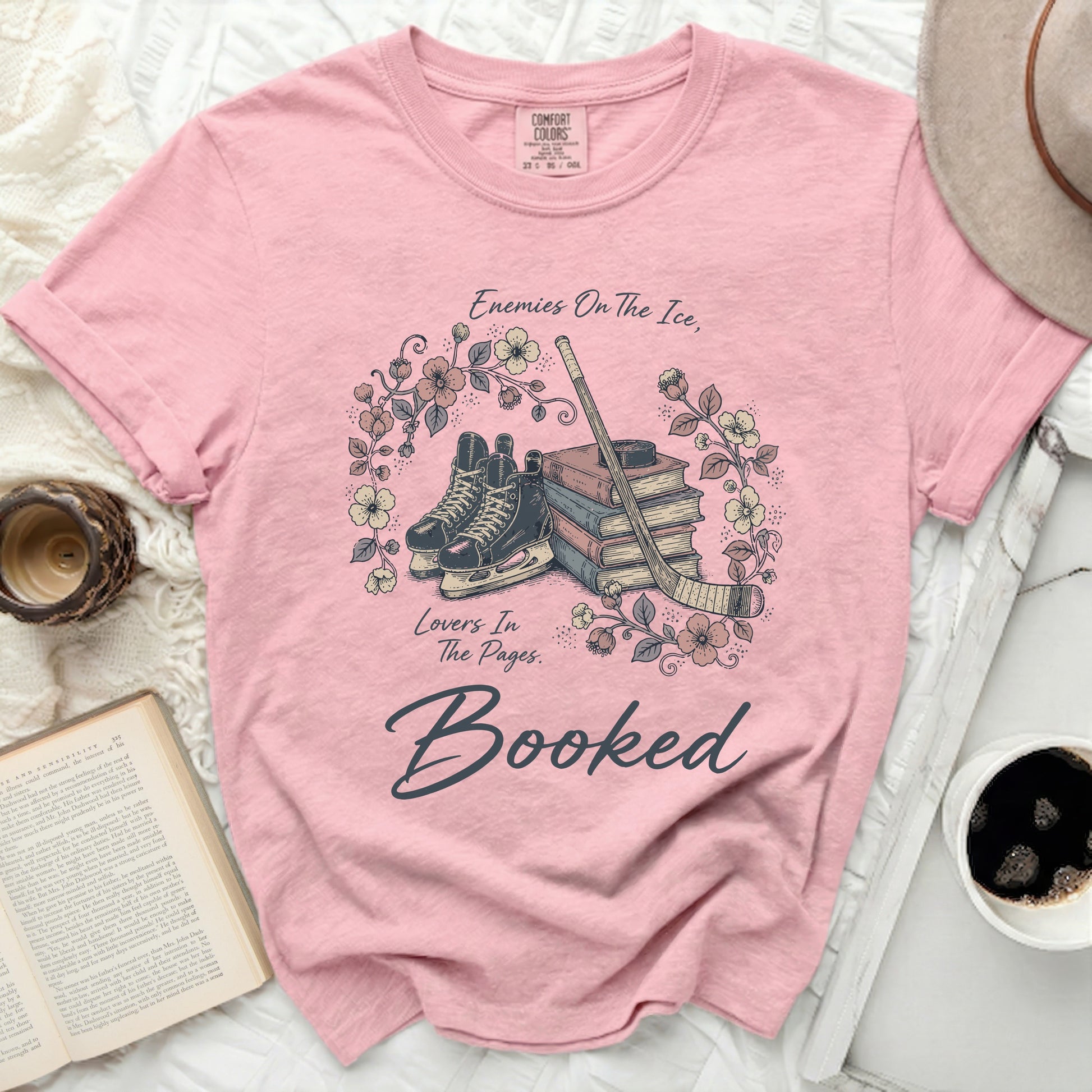 Pink t-shirt with "Enemies On The Ice, Lovers In The Pages. Booked" text and hockey skates.