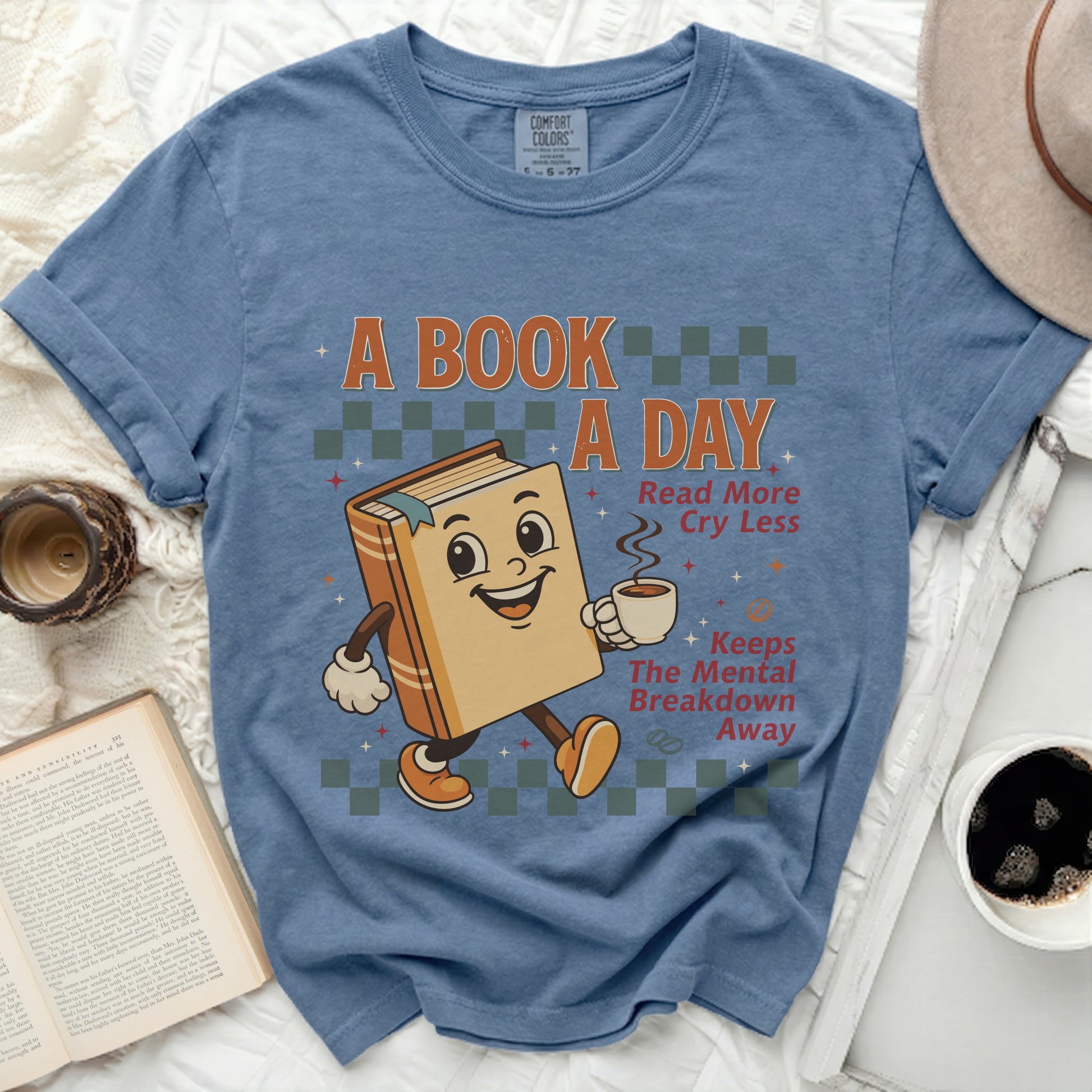 A shirt with a graphic of a book holding a coffee cup and the text "A Book A Day".