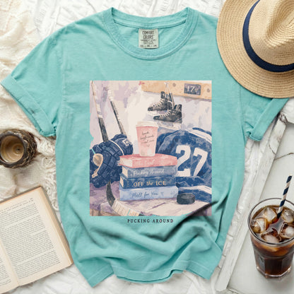 Aqua t-shirt with hockey gear, books, and text "Pucking Around"