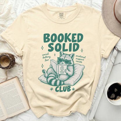 Booked Solid Club t-shirt with raccoon reading a book, "Too Many Plots, Not Enough Sleep".