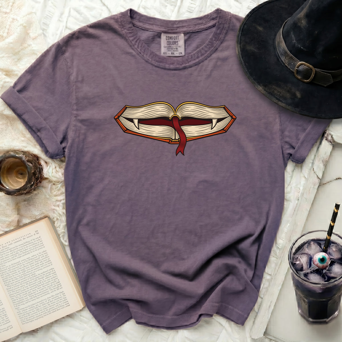 Purple t-shirt with a graphic of an open book with fangs and a bookmark.