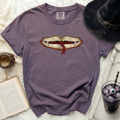 Purple t-shirt with a graphic of an open book with fangs and a bookmark.