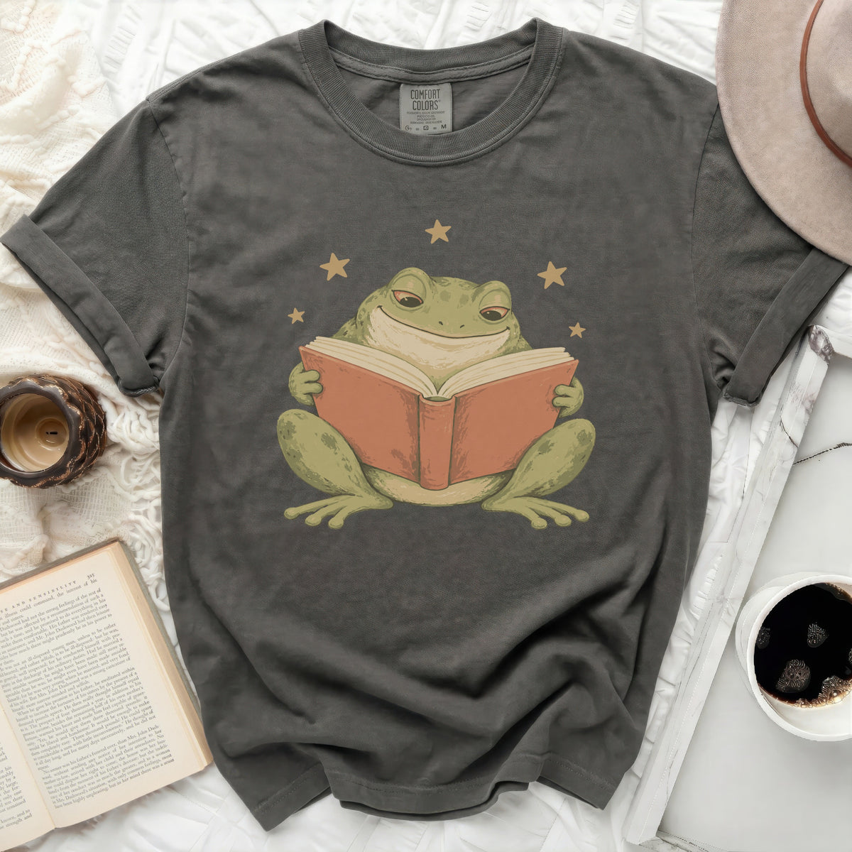 Dark grey Comfort Colors t-shirt with a graphic of a smiling frog reading a book.