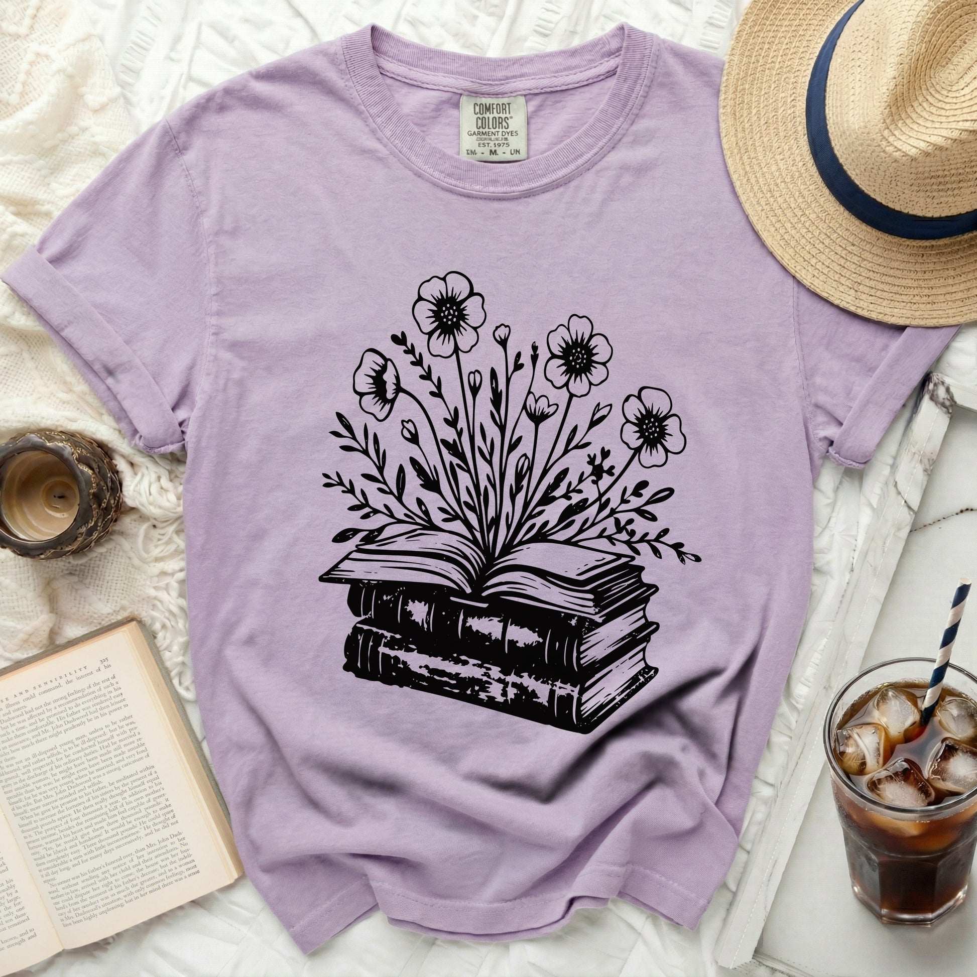 Lavender t-shirt with black floral design emerging from stacked books.