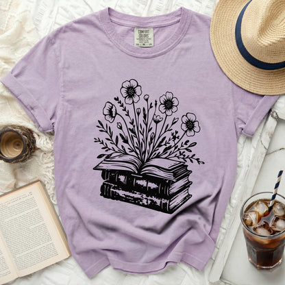 Lavender t-shirt with black floral design emerging from stacked books.