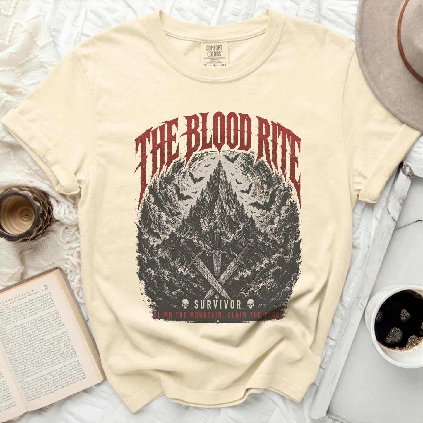 Cream t-shirt with "The Blood Rite Survivor" graphic of mountains, bats, and swords.