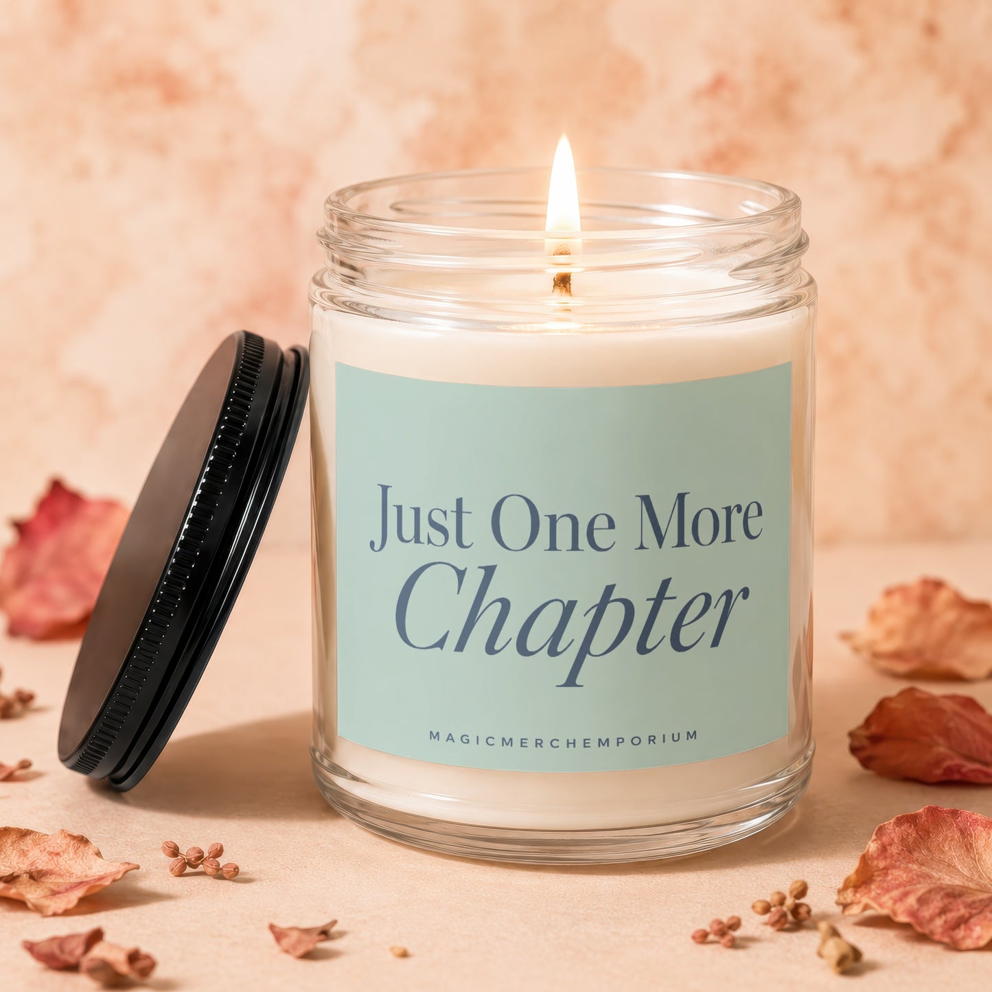 Lit glass candle with teal label reading "Just One More Chapter" and "MAGICMERCHEMPORIUM".